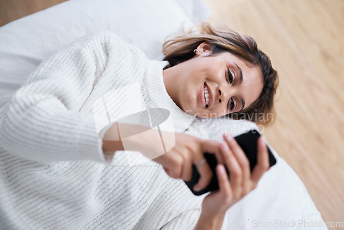 Image of So many people shared my post already. a young woman using her cellphone while lying on her bed.