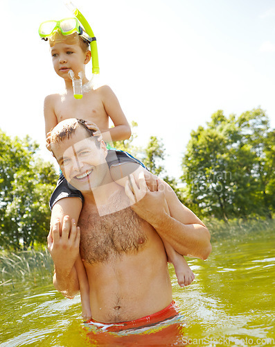 Image of Playing in the lake with my son. Young father standing in a lake carrying his son on his shoulders and smiling.