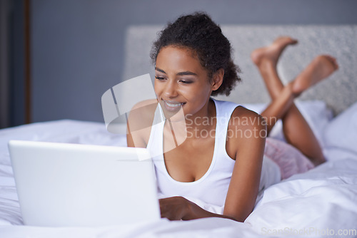 Image of Its time to log off and unwind. young woman using her laptop while lying on her bed.