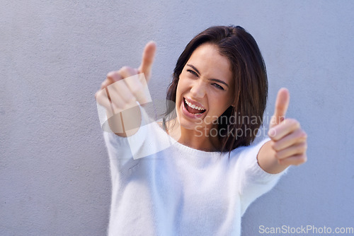 Image of Youre a superstar. Portrait of a happy young woman standing against a gray background and giving thumbs up.