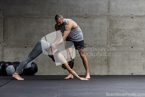 Image of A muscular man assisting a fit woman in a modern gym as they engage in various body exercises and muscle stretches, showcasing their dedication to fitness and benefiting from teamwork and support