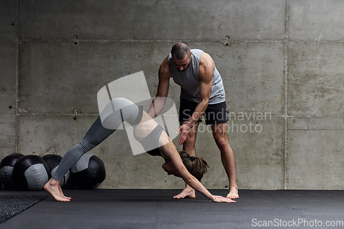 Image of A muscular man assisting a fit woman in a modern gym as they engage in various body exercises and muscle stretches, showcasing their dedication to fitness and benefiting from teamwork and support