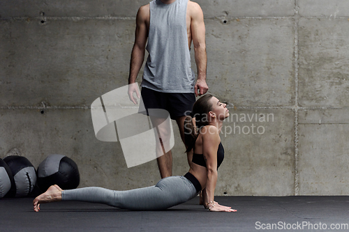 Image of A muscular man assisting a fit woman in a modern gym as they engage in various body exercises and muscle stretches, showcasing their dedication to fitness and benefiting from teamwork and support