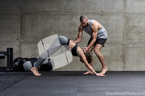 Image of A muscular man assisting a fit woman in a modern gym as they engage in various body exercises and muscle stretches, showcasing their dedication to fitness and benefiting from teamwork and support