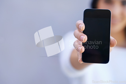 Image of You have to get this phone. Portrait of a young woman standing against a grey background and holding up her mobile phone.