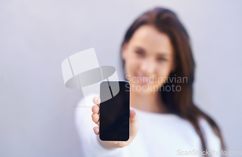 Image of This is the best phone on the market. Portrait of an attractive young woman standing against a gray background and holding up her mobile phone.