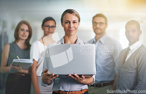 Image of The secret to business success. Portrait of a businesswoman holding a laptop with her colleagues blurred in the background.