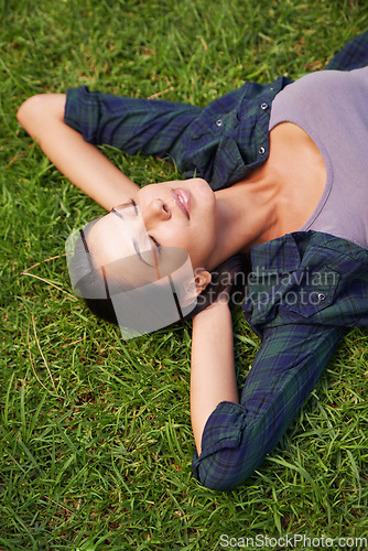 Image of The green grass of home. High angle shot of an attractive young woman lying on the grass.