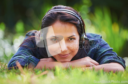 Image of You never know what you might find in the long grass. Portrait of an attractive young woman lying on the grass and listening to music.