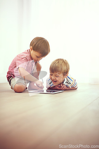 Image of Playtime gone digital. two little boys using a digital tablet together while sitting on the floor.