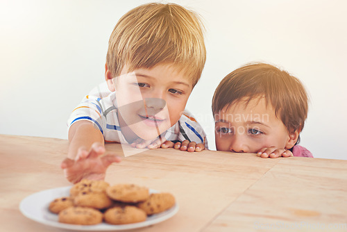 Image of Lets sneak a cookie before dinner. Two little boys sneakily trying to take a cookie from a plate.