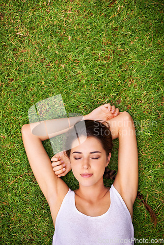 Image of Catching a nap in the sun. Aerial shot of a young woman lying outside on the grass.