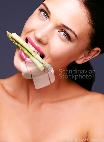 Image of How could you say no to veggies now. Portrait of a woman biting on a bunch of asparagus in studio.