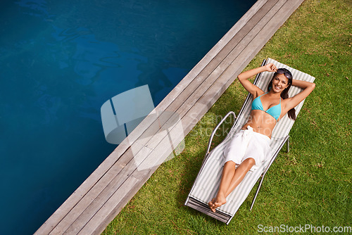 Image of Sunshine and happiness. Portrait of a beautiful young woman relaxing in a lounge chair by a swimming pool.