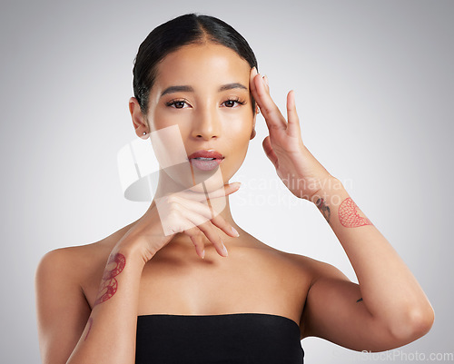 Image of Portrait of a beautiful mixed race woman touching smooth soft skin in a studio. Hispanic model with healthy natural glowing skin looking confident against grey copyspace while doing routine skincare