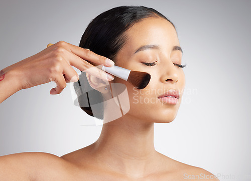 Image of A beautiful mixed race woman posing with a makeup brush during a pamper routine. Hispanic model holding a contouring brush against a grey copyspace background