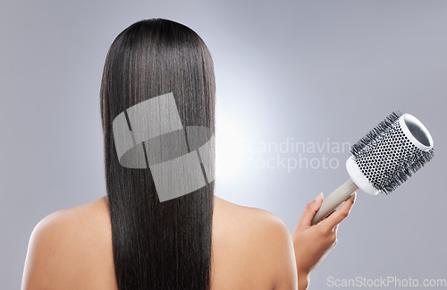 Image of How to get sleeker than sleek hair. Rearview shot of a woman holding a blow-dry brush against a grey background.