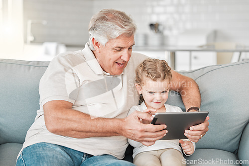 Image of A child needs a grandparent. an adorable little girl using a digital tablet while sitting at home with her grandfather.