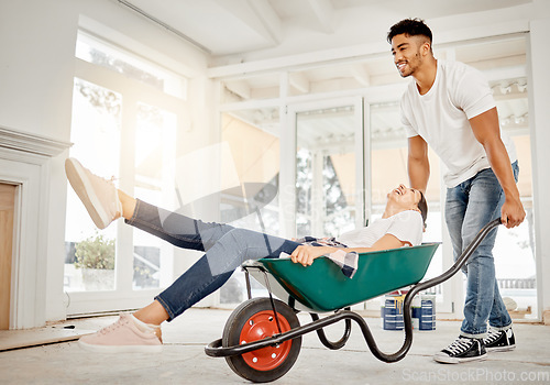 Image of Well always be young at heart. Full length shot of a handsome young man feeling playful while pushing his girlfriend in a wheelbarrow at home.