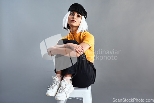 Image of Unique style is everlasting style. Studio shot of a beautiful young woman sitting on a stool against a grey background.