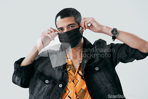 Image of Who said face masks cant be fashionable. Studio shot of a young man putting on a face mask against a grey background.