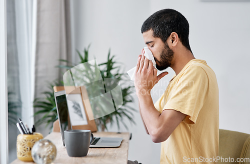 Image of Until he gets better, home is his place of business. a young man blowing his nose while working from home.