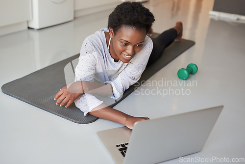 Image of Browsing through a vast digital archive of fitness videos. a young woman using a laptop while exercising at home.