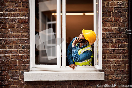 Image of I see the problem. a young engineer talking on his cellphone while looking out the window of a construction site.