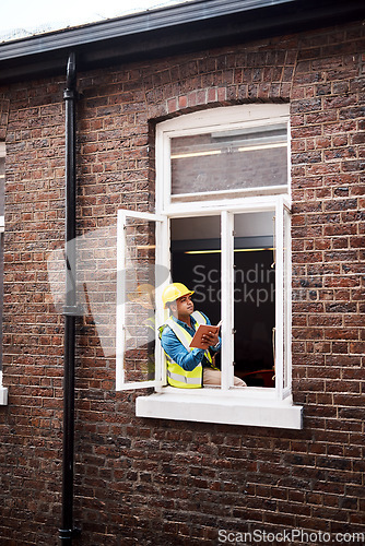 Image of We can definitely expand this window. a engineer making notes while looking out the window of a construction site.