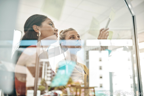 Image of Formulating clear objectives and goals. two businesswomen brainstorming with notes on a glass wall in an office.