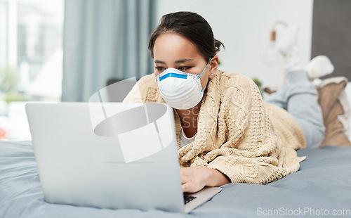 Image of Checking for updates and the latest news on the virus. a woman wearing a mask while lying on her bed with her laptop.