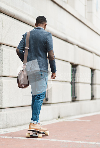 Image of It doesnt matter how you get there, just get there. Rearview shot of a young businessman riding a skateboard through the city.