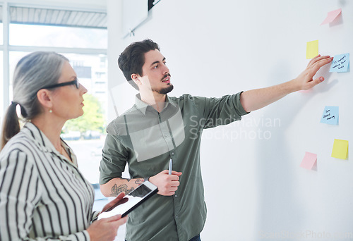 Image of Running through their master plan. two businesspeople brainstorming with notes on a wall in an office.