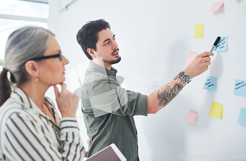 Image of Coming up with a strategy that works. two businesspeople brainstorming with notes on a wall in an office.