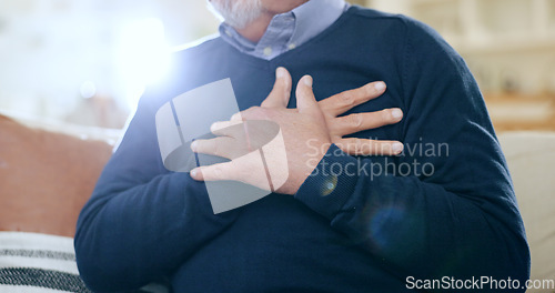 Image of Hands, chest and heart attack with a senior man closeup on a sofa in the living room of his home during retirement. Healthcare, medical and cardiac arrest with an elderly person in pain or agony