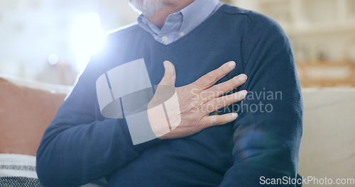 Image of Hand, chest and heart attack with a senior man closeup on a sofa in the living room of his home during retirement. Healthcare, medical and cardiovascular disease with an elderly person in pain