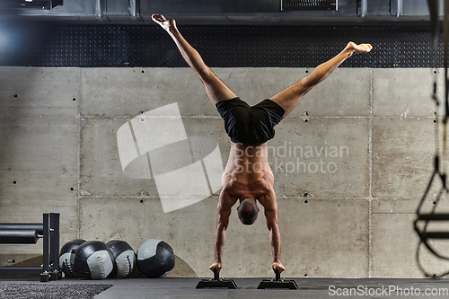Image of A muscular man in a handstand position, showcasing his exceptional balance and body control while performing a variety of exercises to enhance his overall body stability and strength in a modern gym