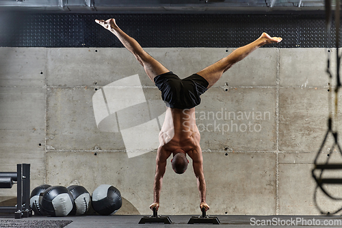 Image of A muscular man in a handstand position, showcasing his exceptional balance and body control while performing a variety of exercises to enhance his overall body stability and strength in a modern gym