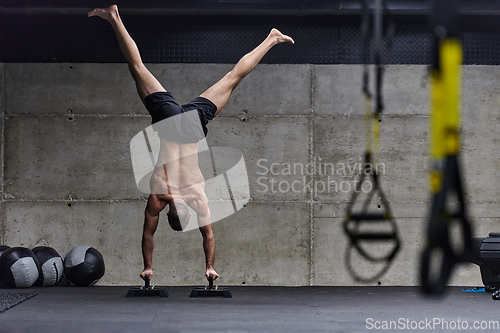 Image of A muscular man in a handstand position, showcasing his exceptional balance and body control while performing a variety of exercises to enhance his overall body stability and strength in a modern gym