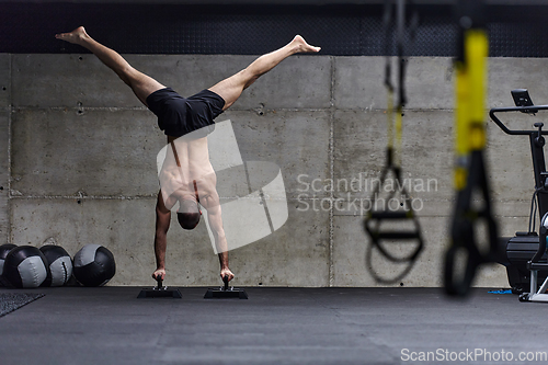 Image of A muscular man in a handstand position, showcasing his exceptional balance and body control while performing a variety of exercises to enhance his overall body stability and strength in a modern gym