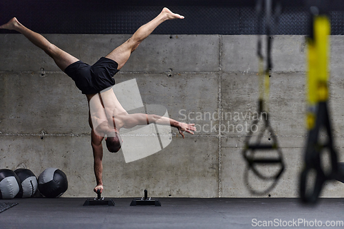 Image of A muscular man in a handstand position, showcasing his exceptional balance and body control while performing a variety of exercises to enhance his overall body stability and strength in a modern gym