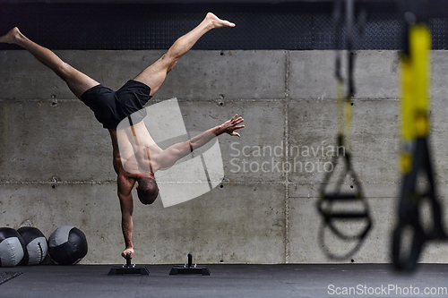 Image of A muscular man in a handstand position, showcasing his exceptional balance and body control while performing a variety of exercises to enhance his overall body stability and strength in a modern gym