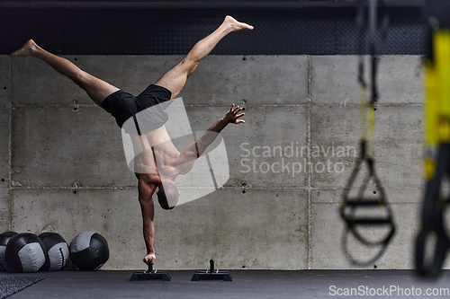 Image of A muscular man in a handstand position, showcasing his exceptional balance and body control while performing a variety of exercises to enhance his overall body stability and strength in a modern gym