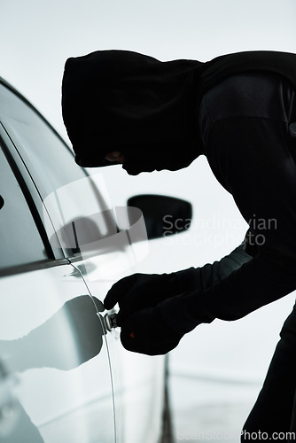 Image of Weaving away until he breaks inside. a masked criminal picking the lock of a car door inside a parking lot.