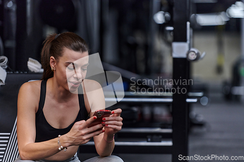 Image of A fit woman in the gym taking a break from her training and uses her smartphone, embracing the convenience of technology to stay connected