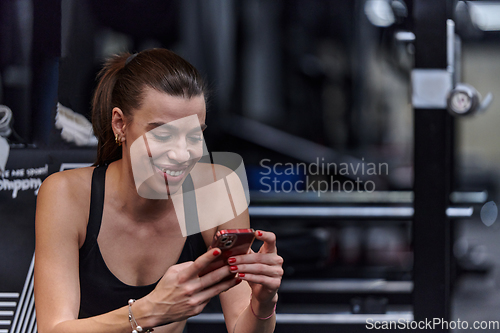 Image of A fit woman in the gym taking a break from her training and uses her smartphone, embracing the convenience of technology to stay connected