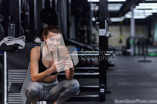 Image of A fit woman in the gym taking a break from her training and uses her smartphone, embracing the convenience of technology to stay connected