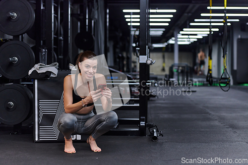 Image of A fit woman in the gym taking a break from her training and uses her smartphone, embracing the convenience of technology to stay connected