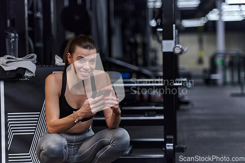 Image of A fit woman in the gym taking a break from her training and uses her smartphone, embracing the convenience of technology to stay connected