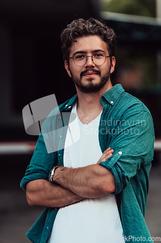 Image of A successful young businessman in a shirt, with crossed arms, poses outdoors, confident expression on his face.